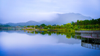 Sejong City, South Korea autumn green space landscape with a hilltop traditional pavilion and reflections over a foggy pond at the National Sejong Arboretum on a rainy morning.