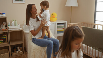 Woman with young son and daughter enjoying time together indoors in a cozy nursery with toys and a...