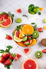 Summer composition with citrus fruits, strawberries and kiwi in bowls on white grid background. Vibrant image. Concept of healthy living and natural food