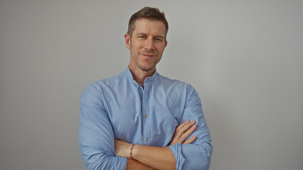 Young man with arms crossed smiling confidently against an isolated white background, showcasing his handsome and attractive appearance in this portrait photo.