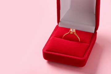 Box with engagement ring on pink background, closeup