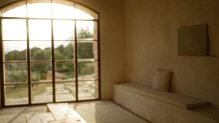 Blurred view inside a luxury mediterranean house with defocused bokeh of an elegant interior and garden visible through large glass windows.