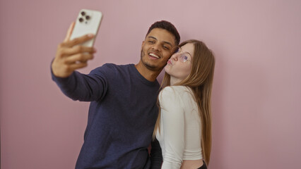 Couple taking selfie together, showing man and woman smiling over isolated pink background,...