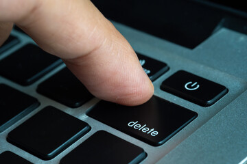Finger of the computer user, he presses the delete button on the computer keyboard.