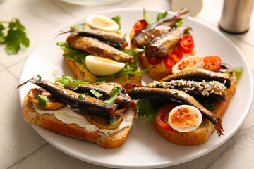 Plate of tasty sandwiches with canned smoked sprats on white tile background