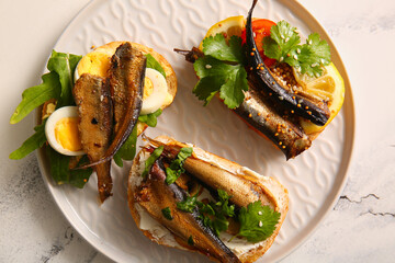 Plate of tasty sandwiches with canned smoked sprats on white marble background