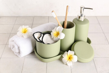 Composition with set of bath supplies, towel and plumeria on white tile table
