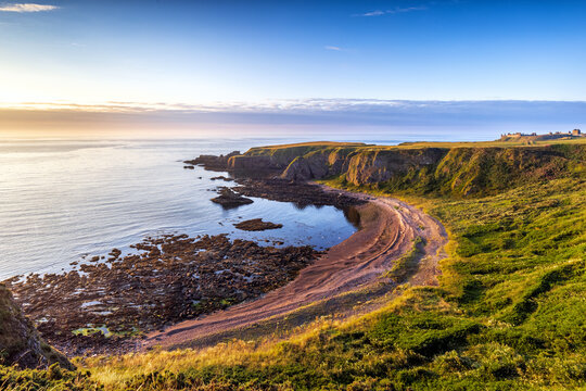 The cliffs and beach at Strathlethan Bay, near Stonehaven, Scotland, with Dunnottar Castle in the distance. Taken just after sunrise.