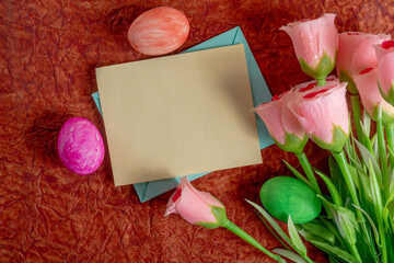 Spring roses and vibrant Easter eggs with a blank card on a rustic background.
