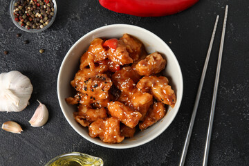 Tasty sweet and sour chicken in bowl with spices on dark background