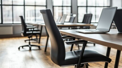 Modern workspace chairs, tables, laptops, large window, and hardwood floor, create a bright office setting