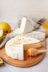 Wooden board with pieces of tasty Camembert cheese on light background