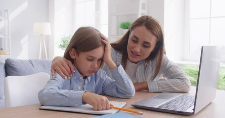 School homework stress, caring young mother, teacher, mentor nanny helping small primary pupil kid son preparing task, sitting together at table, studying homeschooling near laptop online, helping - Powered by Adobe