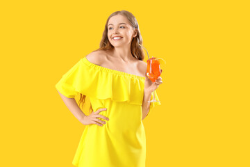 Beautiful young woman with glass of tasty aperol spritz cocktail on yellow background