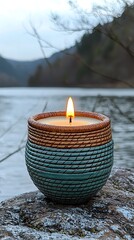 Scented candle in decorative teal and brown container by a lake.