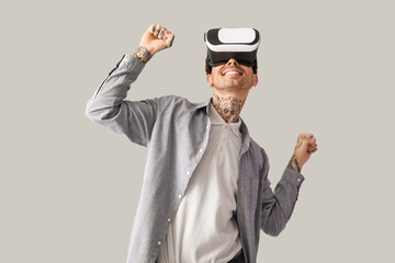 Happy young man using VR headset on grey background