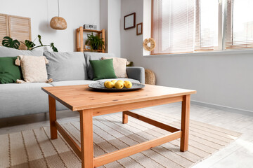 Cozy grey sofa and plate with lemons on wooden coffee table in interior of living room