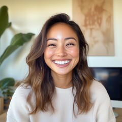 Fototapeta premium Cheerful young woman with wavy hair in casual white sweater smiling brightly in a modern office. Bright daylight, friendly atmosphere, teamwork concept, joyful corporate environment..