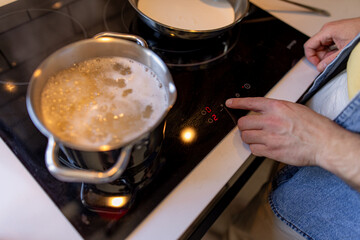 Chef using finger to adjust temperature of modern induction hob while cooking pasta in professional kitchen