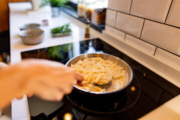 Close-up of a stainless steel pan with penne pasta and creamy sauce cooking on a modern black induction stove