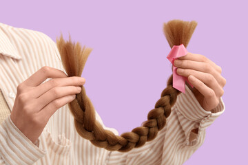 Female hands with braided red hair for donation and pink awareness ribbon on purple background