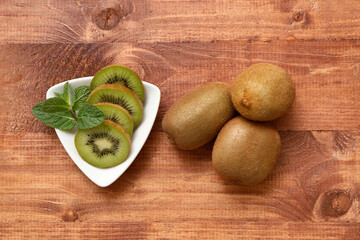 Bowl with slices of fresh kiwi and mint on wooden background
