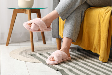 Young woman in pink slippers sitting on armchair in room, closeup