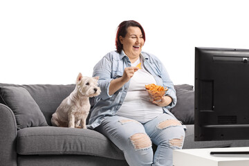 Overweight woman eating crisps and sitting in front of tv with her dog