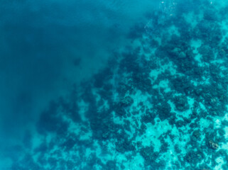 Aerial view of a coral reef beneath turquoise waters, revealing abstract marine textures and vibrant underwater patterns off the coast of Thailand.