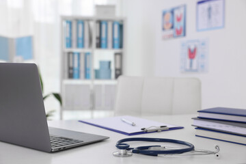 Laptop, stationery and stethoscope on desk in doctor's office, closeup