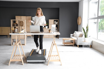 Young businesswoman video chatting on treadmill at table in office