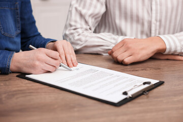 Woman putting signature on document at wooden table, closeup