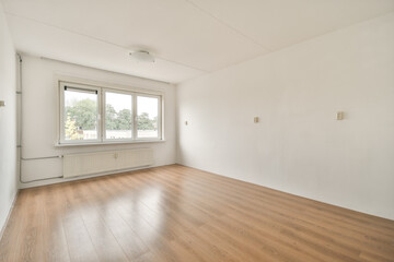 A minimalist interior space featuring a vacant room with a wooden floor and a large window. The walls are white, enhancing the sense of openness and light.