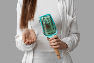 Woman holding brush and clump of hair on grey background. Hair loss concept