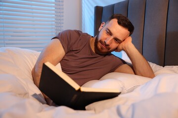Fototapeta premium Young man reading book in bed at home