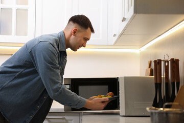 Man putting plate with lunch into microwave in kitchen