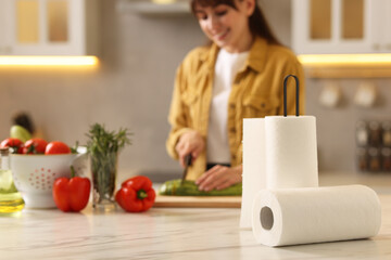 Fototapeta premium Woman cutting zucchini at white marble table in kitchen, focus on rolls of paper towels