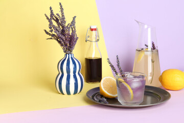Glass and jug of fresh lavender lemonade with flowers on colorful background