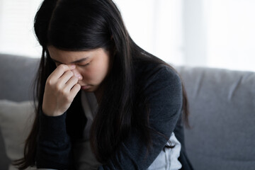 Depressed woman sitting alone on the sofa with hands on head feel stress, sad and worried in the low light environment house