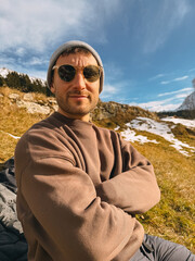 Young hiker enjoying a sunny day in the mountains, wearing sunglasses and a beanie