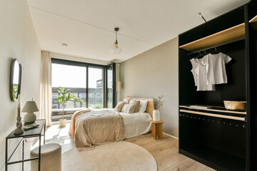 A stylish modern bedroom featuring a large window with natural light, a cozy bed, and minimalist...
