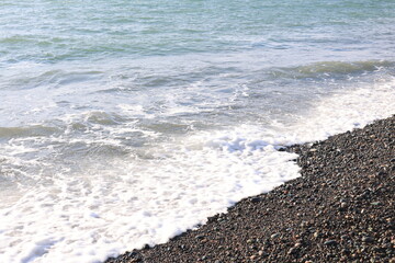 Beautiful pebble beach with calm sea waves and blue sky. Natural seaside landscape with soft sunlight, peaceful atmosphere, and clear water. Summer vacation concept.