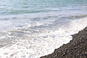 Beautiful pebble beach with calm sea waves and blue sky. Natural seaside landscape with soft sunlight, peaceful atmosphere, and clear water. Summer vacation concept.