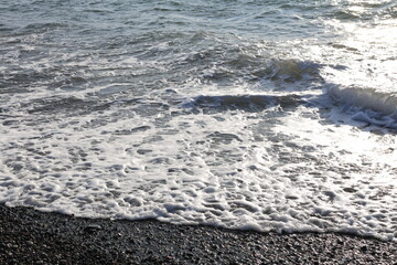 Beautiful pebble beach with calm sea waves and blue sky. Natural seaside landscape with soft sunlight, peaceful atmosphere, and clear water. Summer vacation concept.