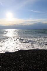 Beautiful pebble beach with calm sea waves and blue sky. Natural seaside landscape with soft sunlight, peaceful atmosphere, and clear water. Summer vacation concept.