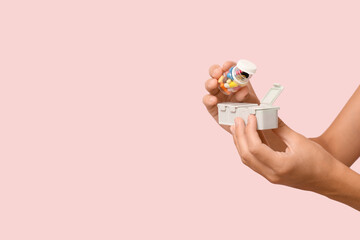 Young woman putting pills from bottle into organizer on pink background