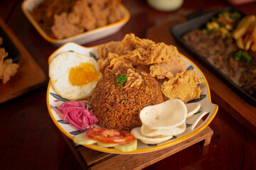 Fried rice with crispy chicken skin, sunny side up, crackers and shallot pickle. Served on white plate. Wooden background. Perfectly for advertising and commercial purpose