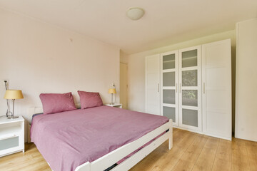 A contemporary bedroom featuring a cozy bed with purple bedding, minimalist decor, and a soothing color palette. Ideal for relaxation and comfort.