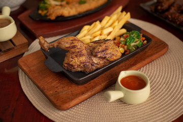 Roasted half chicken with fries and vegetables. Served on black hot plate with barbeque sauce. Landscape angle on wooden table. Perfectly for restaurant advertising