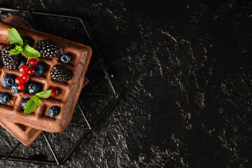 Stand of sweet chocolate Belgian waffles with fresh berries and mint on black background
